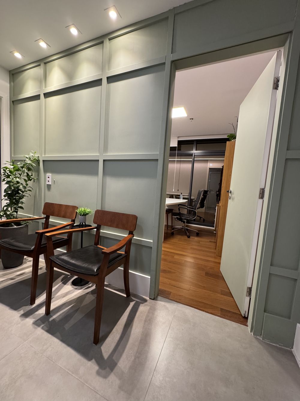 Recepção do consultório, com parede verde e cadeiras de madeira